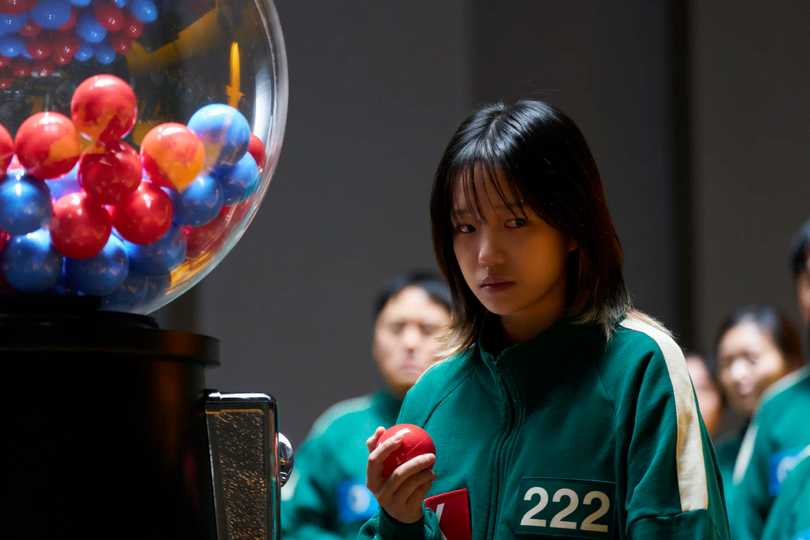 Squid Game Season 3 - Jo Yuri in front of a Large Gumball-like Machine 